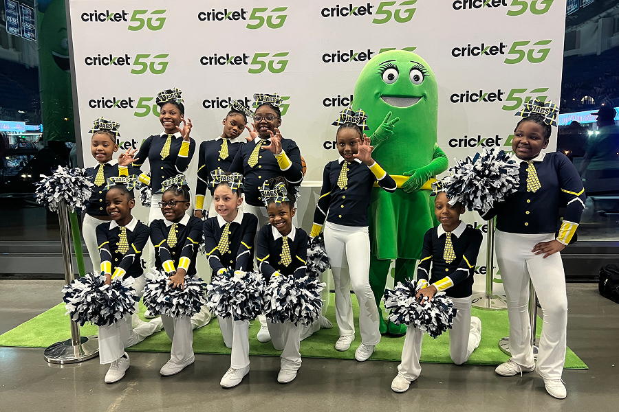 Youth cheerleading squad in uniform posing with the Cricket Wireless mascot in front of a Cricket 5G backdrop at a Georgia State University event