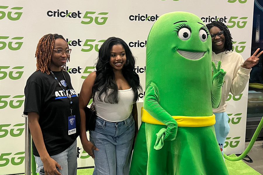 Three Georgia State University fans smiling and posing with the Cricket Wireless mascot in front of a Cricket 5G step-and-repeat banner