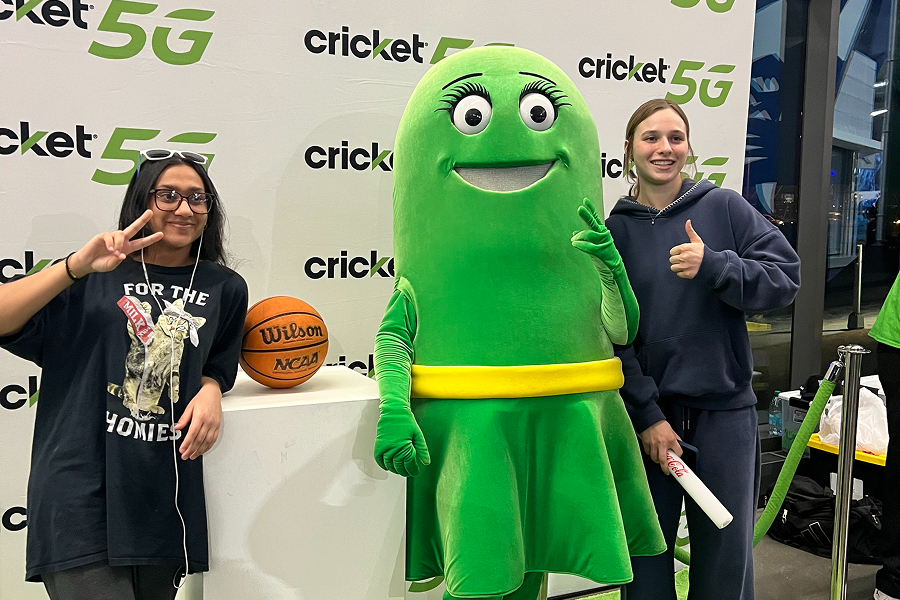 Two GSU fans posing with the Cricket Wireless mascot at a Cricket 5G photo activation, with an NCAA basketball on display