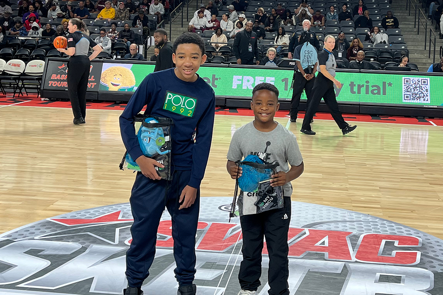 Two young fans standing on the SWAC logo at center court holding Cricket Wireless prize packages during the SWAC Basketball Tournament