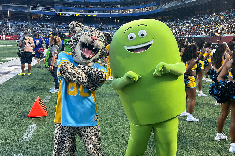 Southern University Jaguar mascot and Cricket Wireless mascot Chip posing together on the sideline during a SWAC football game, with cheerleaders and fans in the background