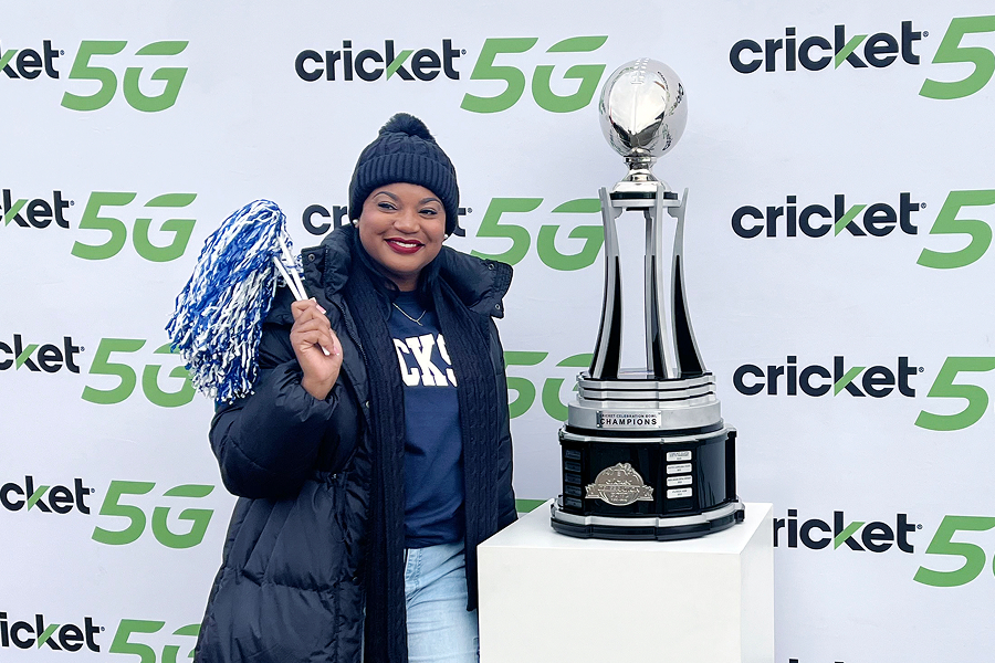 SWAC fan holding blue and white pom-poms and posing next to the Cricket Celebration Bowl Champions trophy in front of a Cricket 5G step-and-repeat banner