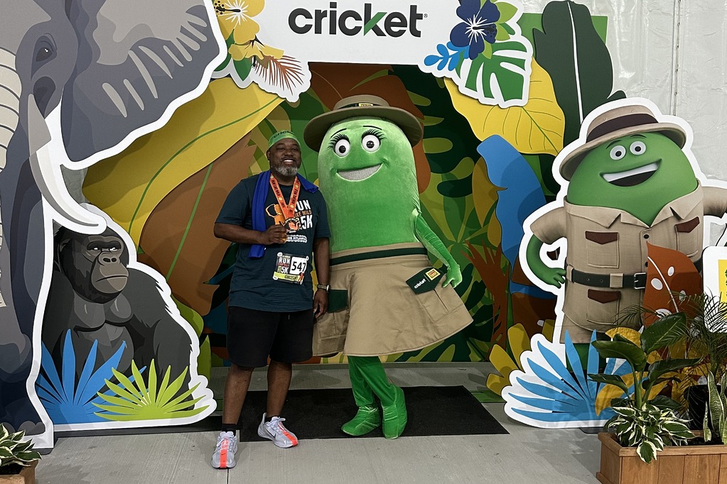 Runner with medal posing with Cricket character Rose at the Cricket booth after the Run Like Wild 5K