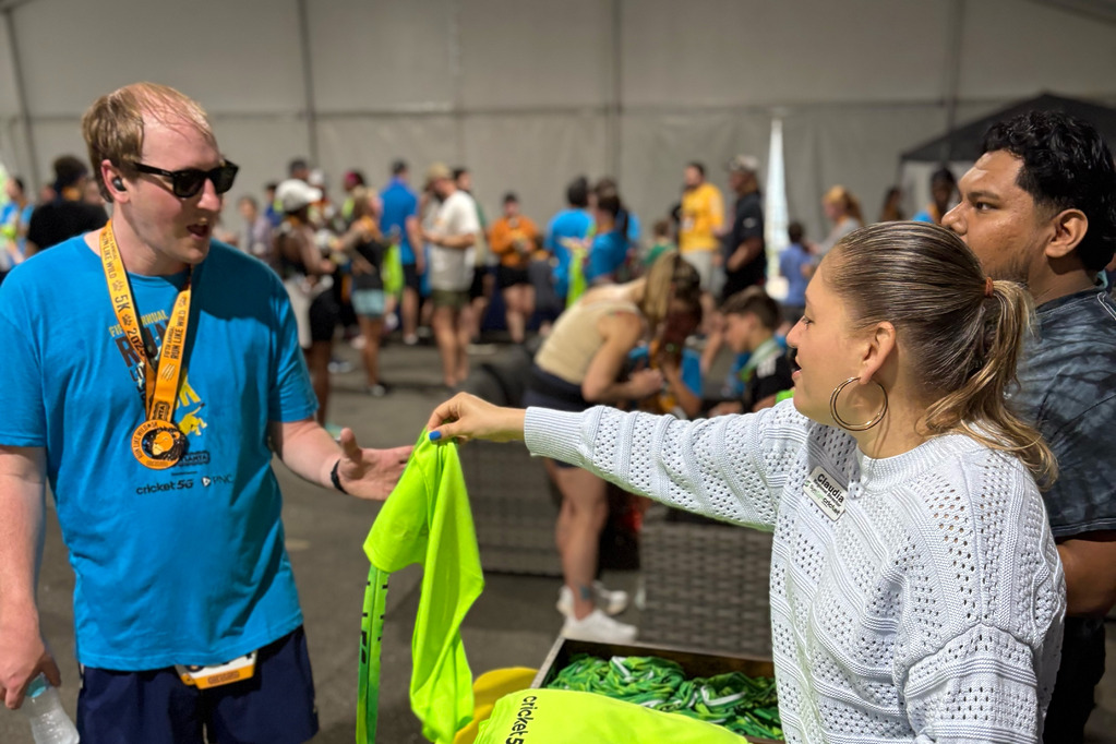 Volunteer handing out bright green Cricket shirts to participants at the Run Like Wild 5K